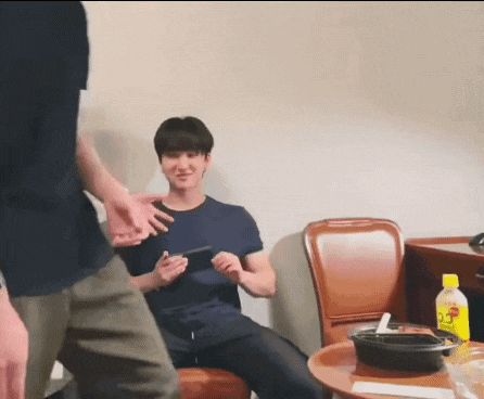 a man is sitting in a chair playing a video game while another man stands behind him .