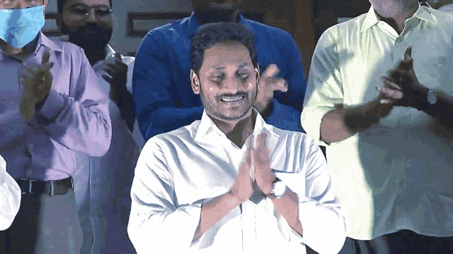 a man in a white shirt with his hands folded in front of a group of people