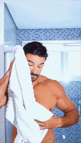 a shirtless man wipes his face with a white towel in a bathroom