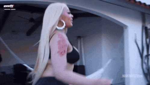a woman with blonde hair and a tattoo on her arm is standing on a balcony .