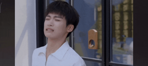 a young man in a white shirt is making a funny face while standing in front of a window .