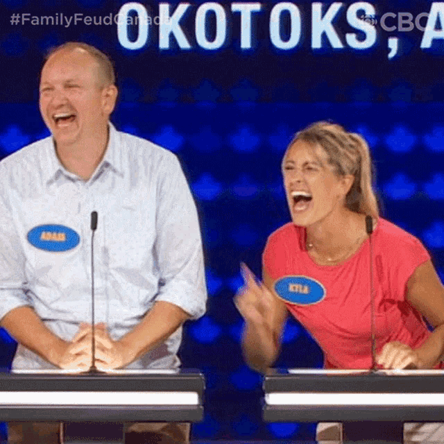a man and a woman are laughing in front of a sign that says okotoks