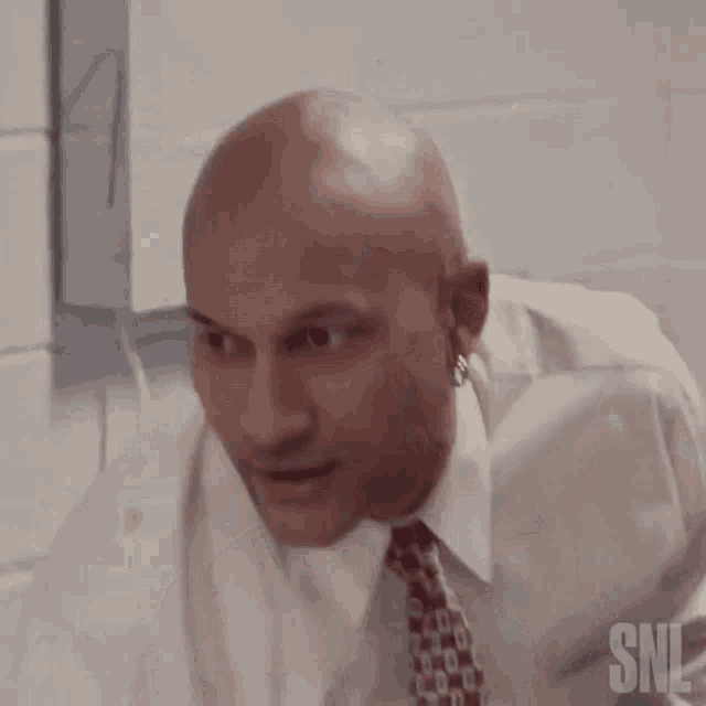 a bald man in a white shirt and tie is talking to another man .