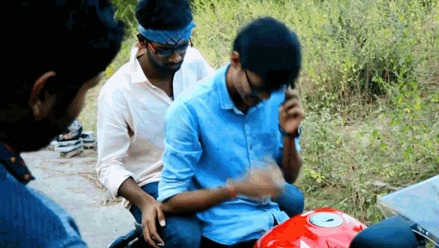 a man in a blue shirt is sitting on a red motorcycle talking on a cell phone