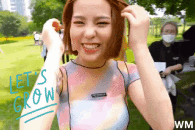 a woman in a tie dye shirt is smiling and holding a strawberry in her hand .