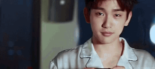 a young man in a white shirt is holding a cell phone in his hand and looking at the camera .