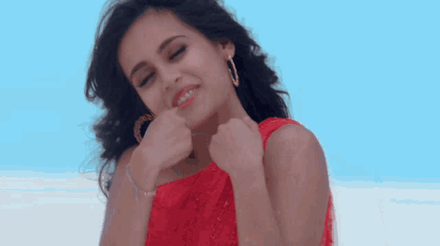a woman in a red dress and hoop earrings smiles