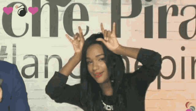 a woman making a devil horns sign in front of a sign that says che pira