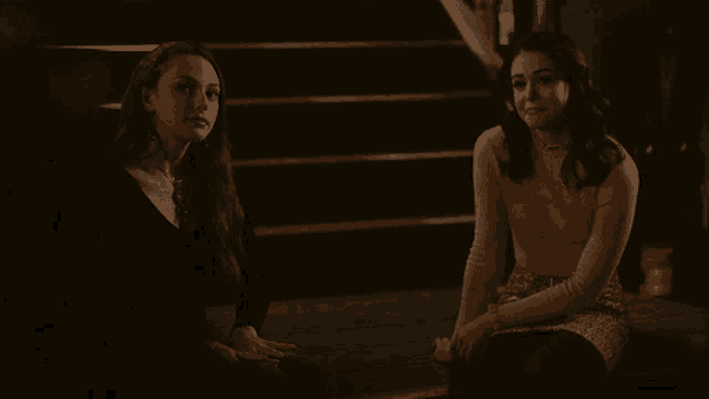 two women are sitting next to each other and smiling in a dark room