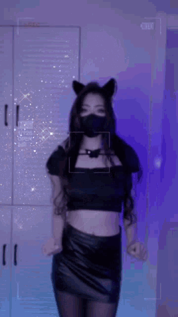 a woman wearing a black mask and cat ears is dancing .