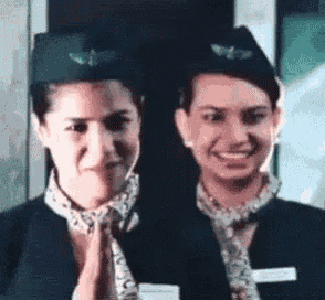 two stewardesses are standing next to each other and smiling for the camera .
