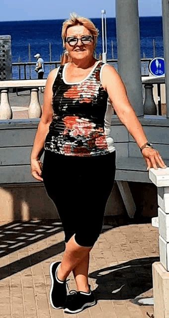 a woman wearing glasses and a tank top is standing on a sidewalk next to a railing .