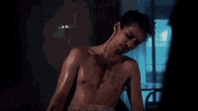 a man without a shirt is laying on a bed with blood on his chest .