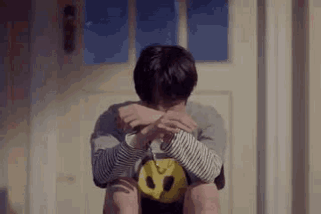 a young man is sitting on a porch with his head down and his hands on his knees .