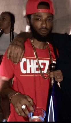 a man wearing a red cheez shirt holds a bottle of wine