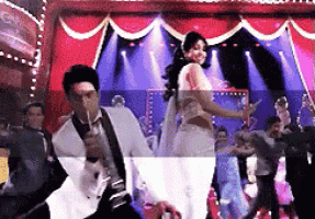 a man in a tuxedo is singing into a microphone while dancing with a woman in a white dress