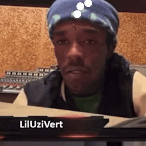a man wearing a blue beanie is sitting in front of a sign that says lil uzivert