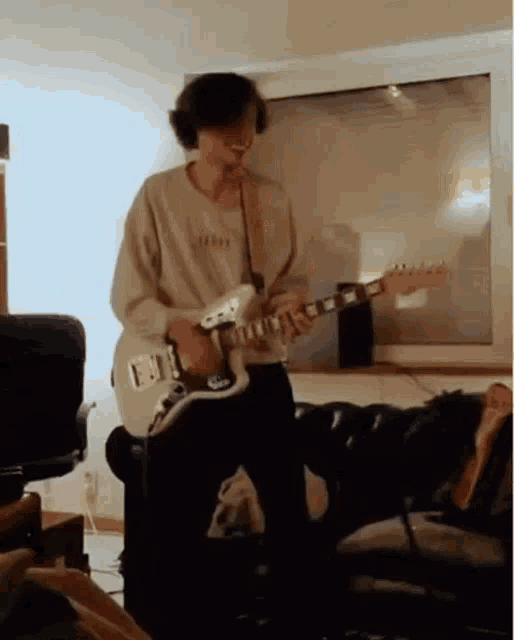 a young man is playing a white electric guitar in a room .