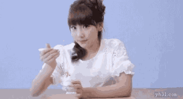 a girl is sitting at a table eating ice cream from a spoon .
