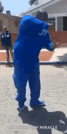 a man in a blue shirt and blue pants is walking down a street .