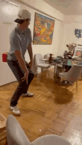 a man is dancing in a living room with a painting on the wall behind him .
