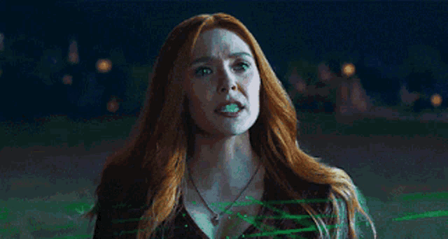a woman with red hair and a necklace is standing in front of a green background .