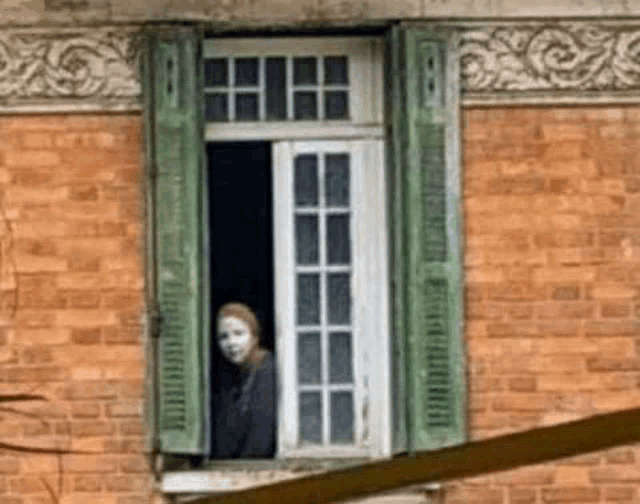 a woman in a mask looks out of a window with green shutters