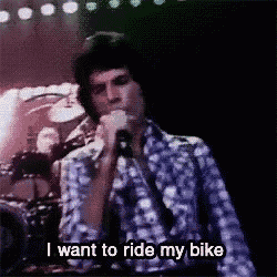 a man is singing into a microphone on a stage and says `` i want to ride my bike '' .