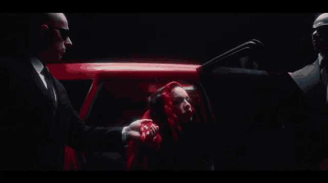 a woman in a red dress is being escorted into a red car by two men in suits