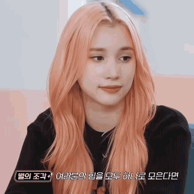 a woman with long pink hair is wearing a black shirt with korean writing on it