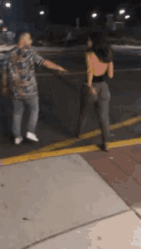 a man and a woman are standing on a sidewalk at night .
