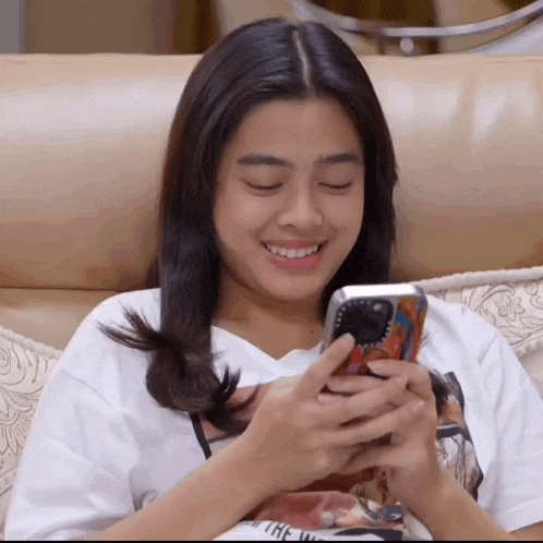 a woman is sitting on a couch looking at her phone and smiling