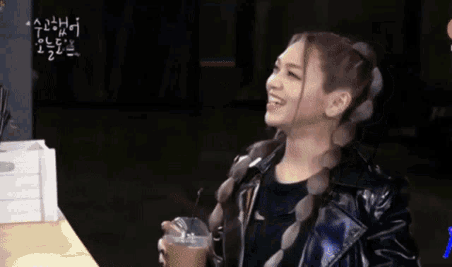 a woman in a black leather jacket is holding a cup of coffee and smiling .