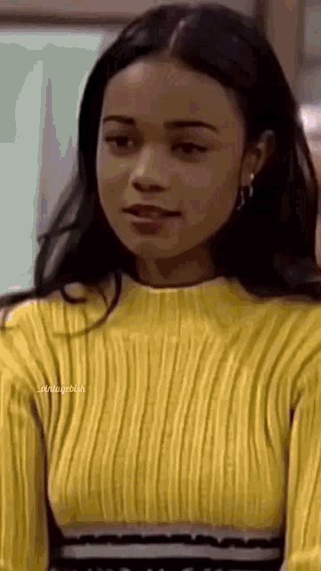 a woman is wearing a yellow sweater and earrings and looking at the camera .
