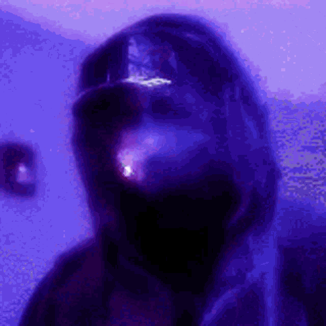 a man wearing a hoodie and a hat is smoking a cigarette in a dark room