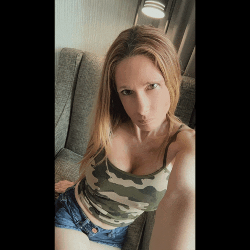 a woman sitting on a couch wearing a camo tank top