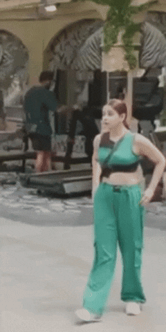 a woman in a crop top and green pants is standing in front of a treadmill .