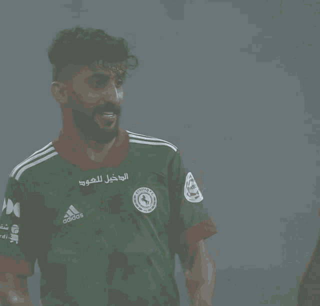 a soccer player wearing a green adidas jersey applauds