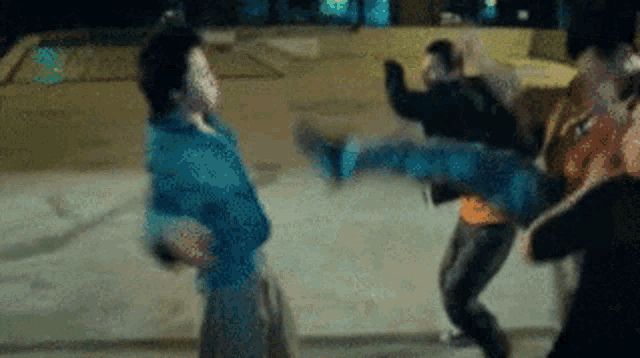 a woman is kicking a man in the face while a group of people are fighting .
