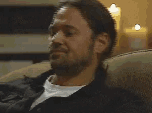 a man with a beard is sitting on a couch with a candle in the background