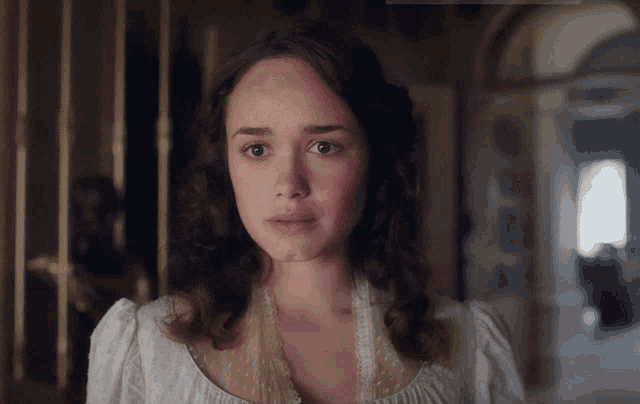 a woman in a white dress looks at the camera with a sad look on her face