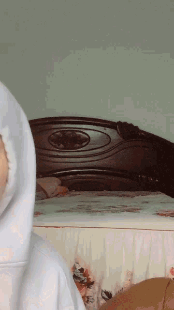 a woman in a white hoodie stands in front of a bed