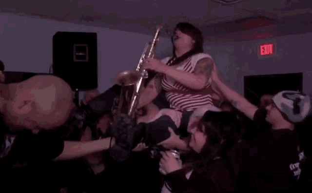 a woman playing a trombone is being lifted in the air by a crowd in front of a red exit sign