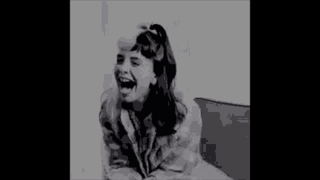 a black and white photo of a woman sitting in a chair laughing .