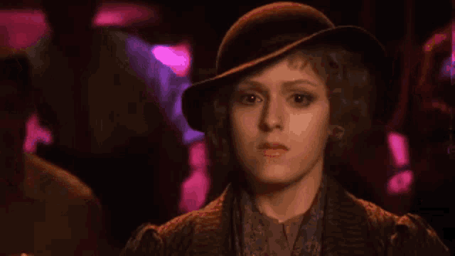 a woman wearing a hat and a brown jacket is standing in a dark room .