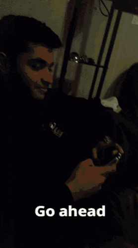a man sitting on a couch holding a cell phone with the caption go ahead