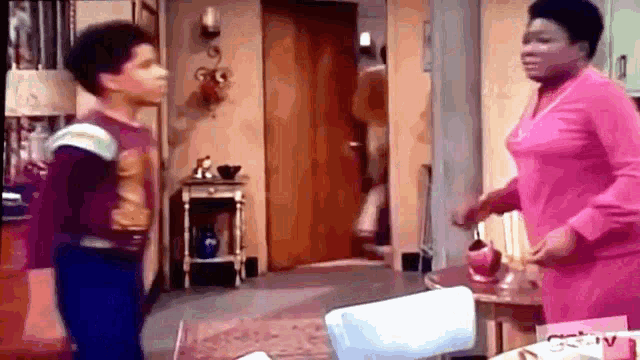 a woman in a pink dress is standing next to a boy in a room .