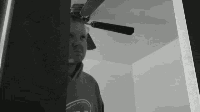 a man is standing in a room with a ceiling fan behind him