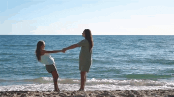 a woman and a girl are holding hands on the beach near the ocean .