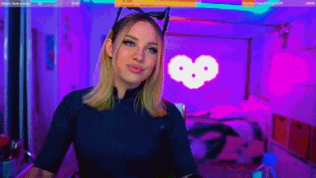 a woman wearing a cat ear headband is standing in front of a heart shaped light .